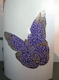 Mosaik aus blauen und schwarzen Fliesen in Form eines Schmetterlings auf einer weißen Wand.