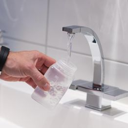 Ein Hand füllt eine Flasche mit Wasser aus einem modernen Wasserhahn.