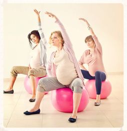 Drie zwangere vrouwen doen rek- en strekoefeningen op roze fitnessballen in een lichte zaal.
