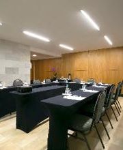 Sala de conferência vazia com mesas retangulares cobertas por toalhas pretas e cadeiras alinhadas.