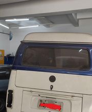 Kombi estacionada em oficina, ao lado de um carro cinza.