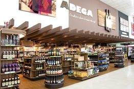 Adega bem iluminada com prateleiras cheias de garrafas de vinho e bebidas variadas.