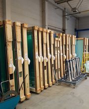 Glasscheiben in Holzrahmen lagern in einer Halle. Daneben stehen mehrere Gestelle und Geräte.