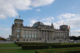Reichstagsgebäude in Berlin bei Tageslicht, mit Wolken am Himmel und Flaggen auf Türmen.