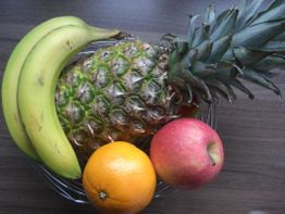 Obstschale mit Ananas, Banane, Orange und Apfel auf einem Holztisch.