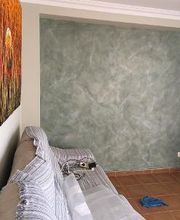 Sala con pared verde, sofá cubierto y cuadro. Suelo de baldosas, mopa azul en el suelo.