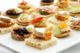 Assortiment de canapés variés sur un plateau blanc, garnis de fromage, fruits secs et légumes.