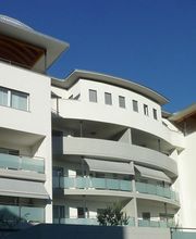 Moderne, mehrstöckige Wohnanlage mit weißen Fassaden und großen Balkonen unter blauem Himmel.