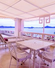 Terraza con sillas y mesa, vista al mar y montañas en el fondo, clima soleado.