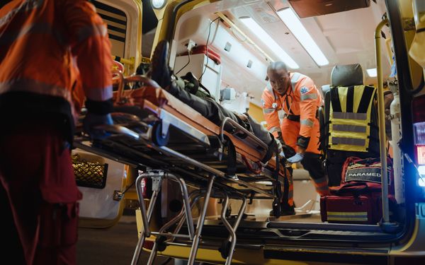 zwei Sanitäter schieben einen Patienten auf einer Liege in ein Rettungsfahrzeug.