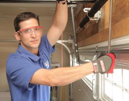 Technician in blue shirt fixing a garage door while wearing safety glasses and gloves.