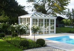 Weißer Wintergarten neben einem Pool im Garten mit blühendem Strauch.