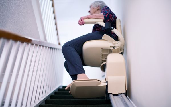 Eine Rentnerin sitzt auf ihrem Treppenlift und fährt ihre Treppe hinauf.