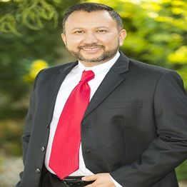 Man in a black suit and red tie smiling outdoors.