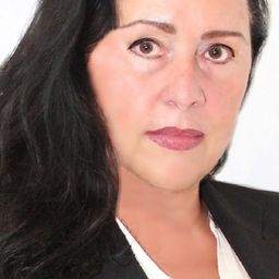 Frau mit langen, dunklen Haaren und weißem Hemd unter einem schwarzen Blazer.