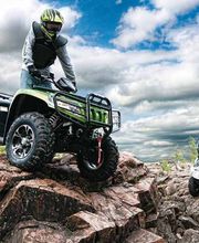 Personas conduciendo cuatrimotos sobre rocas bajo un cielo nublado y azul.