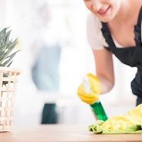 Person cleaning a table with a spray bottle, wearing yellow gloves.