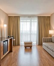 Sala de estar com sofá, TV, cortinas, luminária e piso de madeira. Móveis em tons neutros.