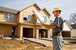 Construction worker in a hard hat examines blueprints at a residential building site.