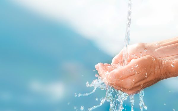 Hände werden vor verschwommenen blauen Hintergrund unter fließendes Wasser gehalten.