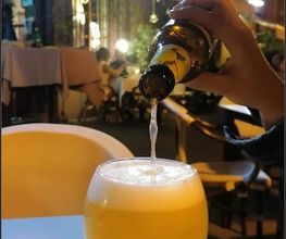 Persona sirviendo cerveza en una copa en una terraza iluminada por la noche.