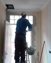 Persona pintando pared en escalera dentro de una habitación. Lleva gorra blanca y ropa de trabajo.