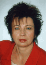 Porträt einer Frau mit kurzen, dunklen Haaren in einem roten Blazer vor neutralem Hintergrund.