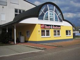Gelbes Gebäude mit "Kunst & Event-Haus" Schild, modernem Dach und gepflastertem Vorplatz.