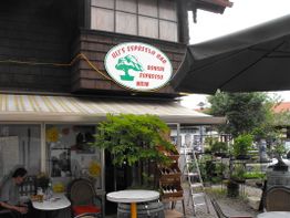 Außenansicht von Ulis Espresso Bar mit Tischen, Stühlen und einem großen Sonnenschirm.