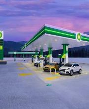 Gasolinera moderna al atardecer con autos estacionados y montañas al fondo.