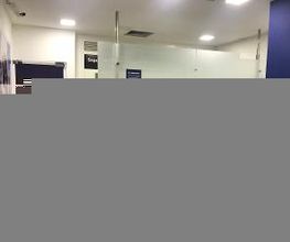 Saguão de um banco com portas de vidro e placas de sinalização. Luzes de teto visíveis.
