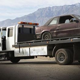 Tow truck carrying an old car with mountains in the background.