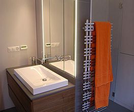 Modernes Badezimmer mit Waschbecken, Spiegel und Handtuchhalter mit orangefarbenem Handtuch.