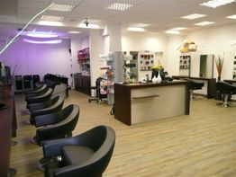 Moderner Friseursalon mit leeren schwarzen Stühlen, Empfangstresen und Regalen mit Produkten.