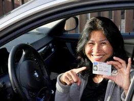 Frau im Auto zeigt lächelnd ihren Führerschein.