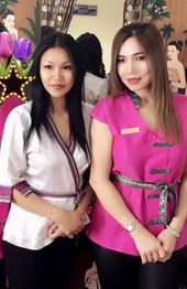 Zwei Frauen in traditioneller Kleidung posieren lächelnd vor einem Spiegel mit Deko im Hintergrund.