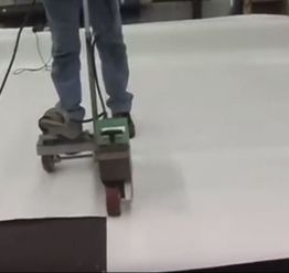 Person using a machine to smooth a large white surface, wearing jeans and gray shoes.
