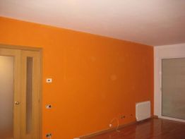 Habitación con pared naranja, puerta de madera y ventana cerrada con persiana bajada.