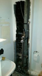 Ein freigelegtes Rohrsystem in einer Wand neben einem Waschbecken und einem Toilettenpapierhalter.