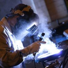 Person welding metal with protective gear, bright sparks and smoke visible.