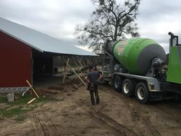 Concrete truck unloading at a construction site beside a red barn structure.