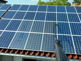 Solarpaneele werden mit einem Reinigungsstab auf einem Hausdach gereinigt.