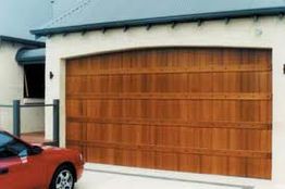 Wooden garage door on white building, red car parked in front.