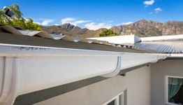 White gutter on a metal roof with mountains in the background under a blue sky.