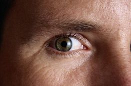 Nahaufnahme eines offenen menschlichen Auges mit brauner Iris und klaren Details der Haut.