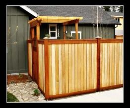 Wooden privacy fence with a small gate and pergola next to a gray house.