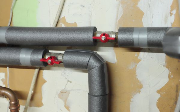 Isolierte Wasserleitungen vor einer verputzen Kellerwand.