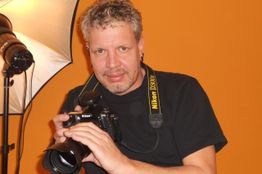 Mann mit Kamera und Kameraausrüstung im Fotostudio, orange Hintergrund.