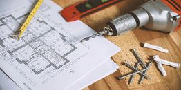 Blueprint, drill, screws, and tools on wooden table for construction project.