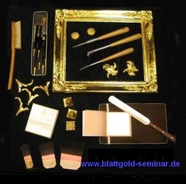 Werkzeuge und Materialien zur Vergoldung: Pinsel, Blattgold, Zierstücke und ein vergoldeter Rahmen.